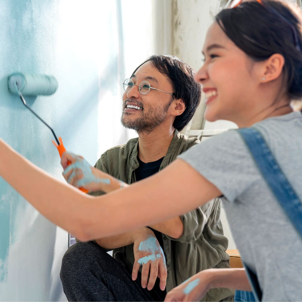 A couple is smiling while painting a wall.
