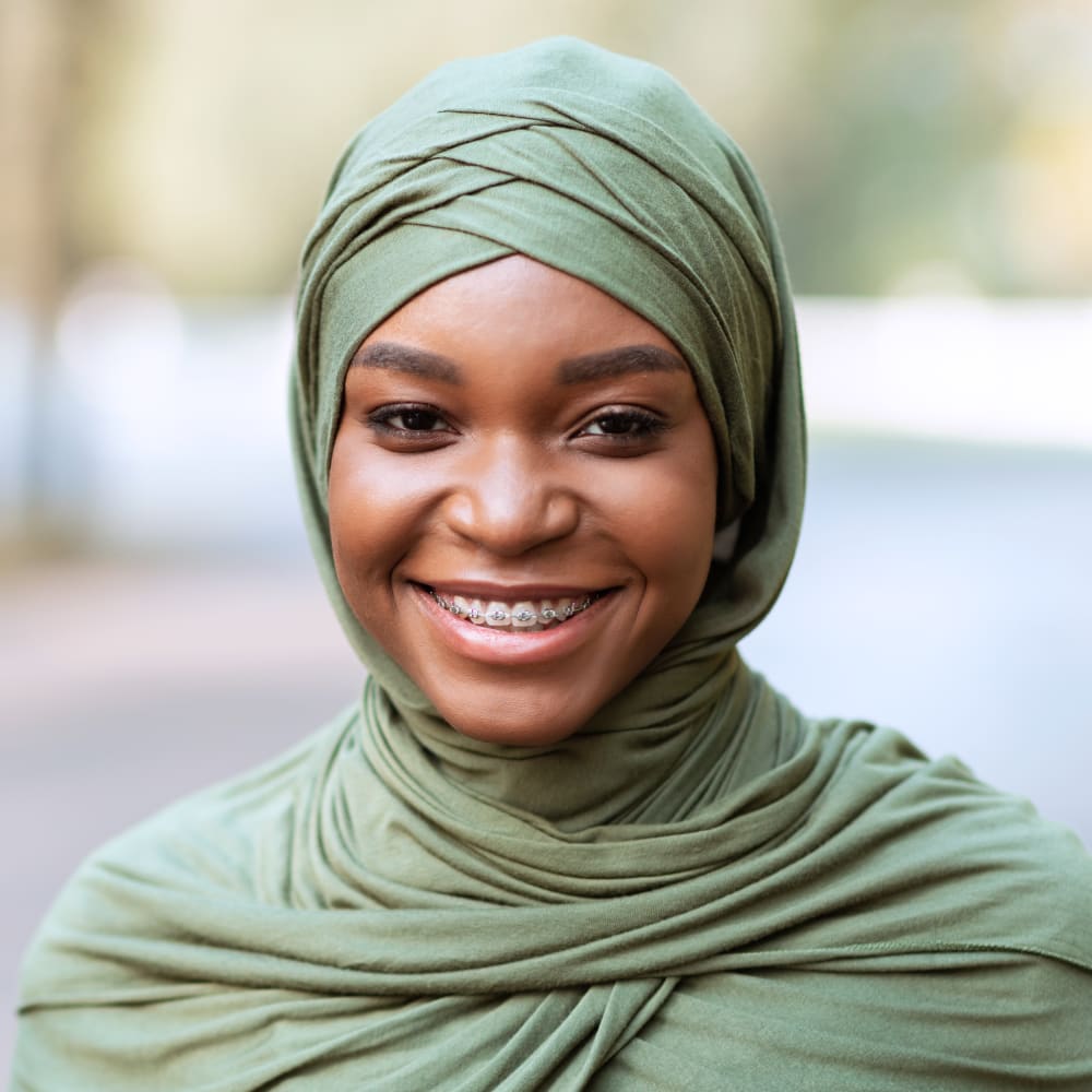 A woman with a green scarf is smiling, showing off braces.