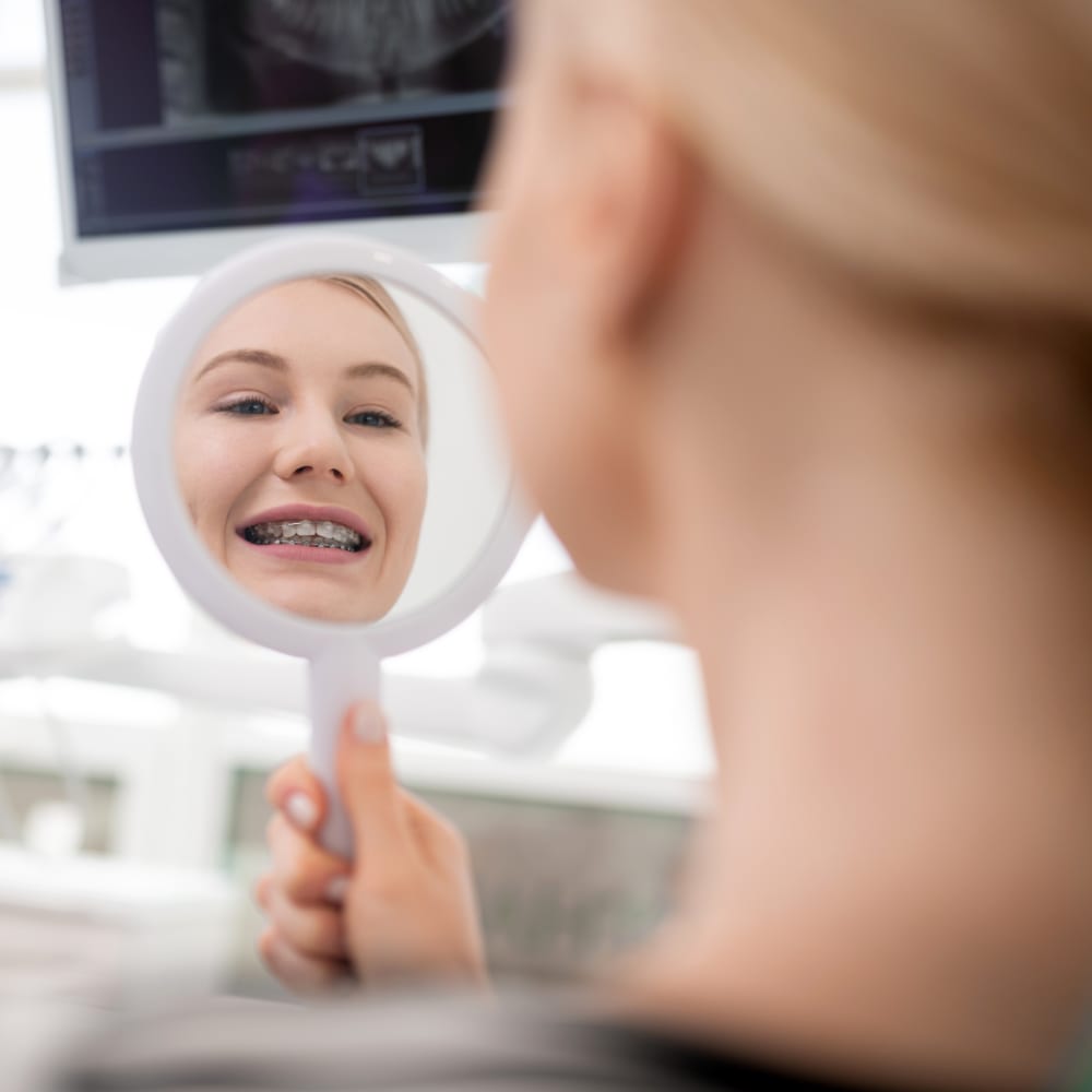A woman looks at her braces in a mirror.