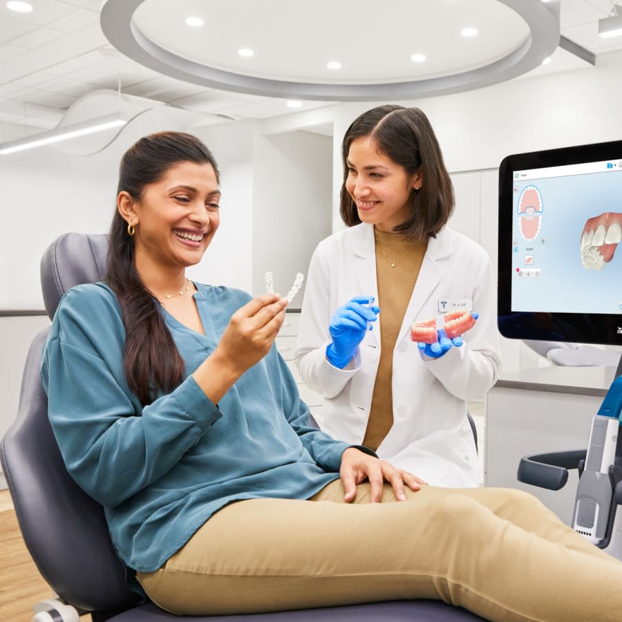 A dentist and a patient review the patient's oral health. A screen shows a digital rendering of her upper teeth.