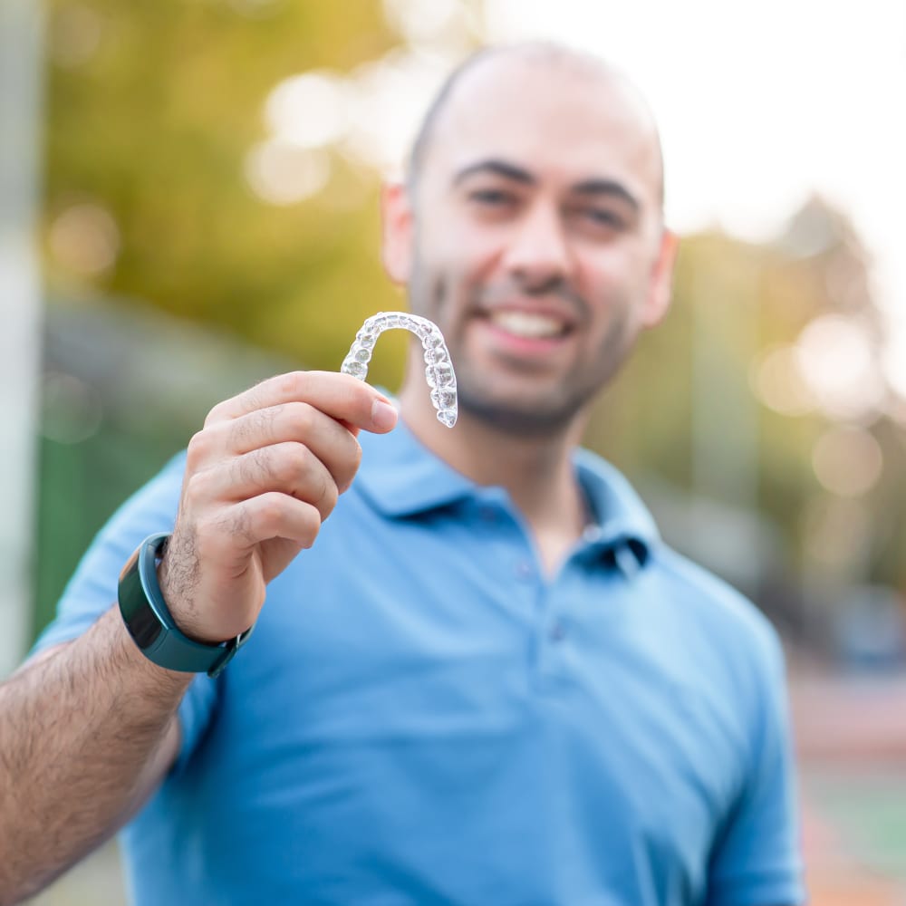 A man holds up an Invisalign aligner tray.