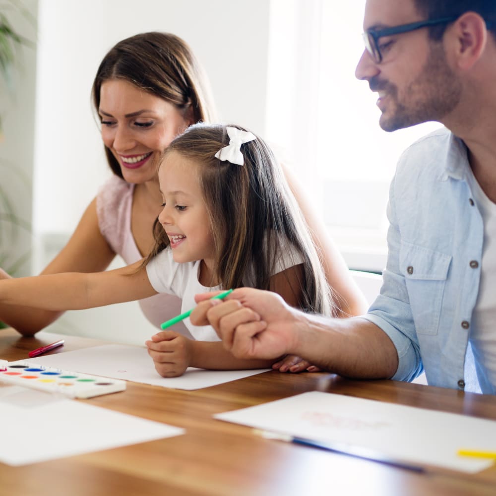 A young girl colors with her parents on either side of her.