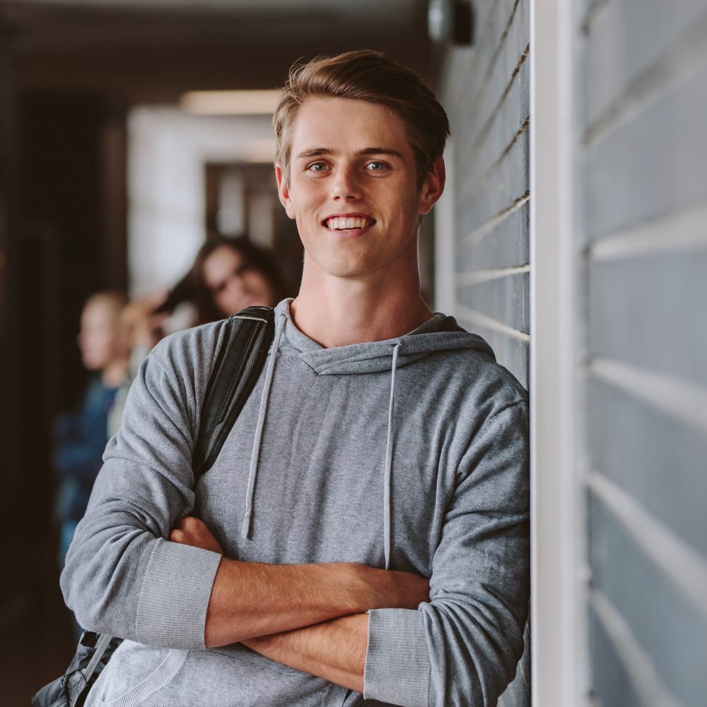 A young man in a grey sweater is smiling.