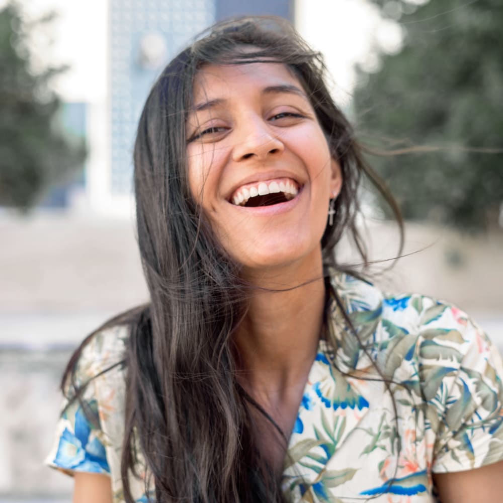 A young woman is smiling. The wind is moving her hair around her face.