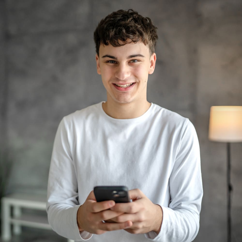 A young boy is smiling while using his phone.
