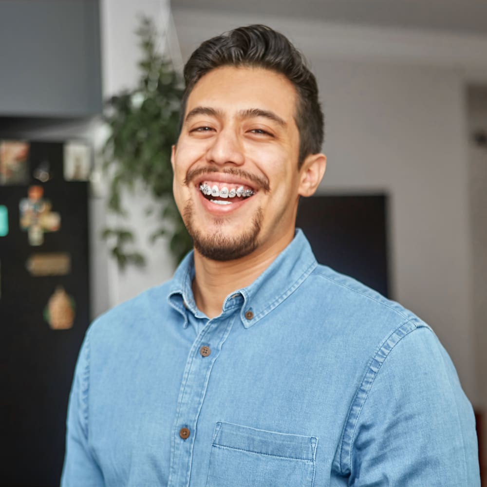 A man in a denim shirt is smiling, revealing a mouth of braces.
